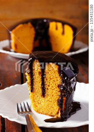 A slice of Brazilian carrot cake with a glossy, dripping chocolate frosting, served on a white plate with a rustic, blurred background A slice of Brazilian carrot cake with a glossy, dripping chocolate frosting, served on a white plate with a rustic, blurred background 135431180