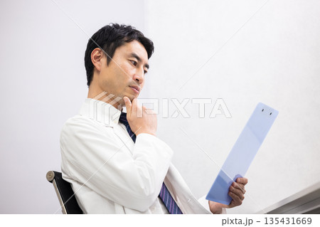 真剣な表情でカルテを読む白衣姿の男性医師 135431669
