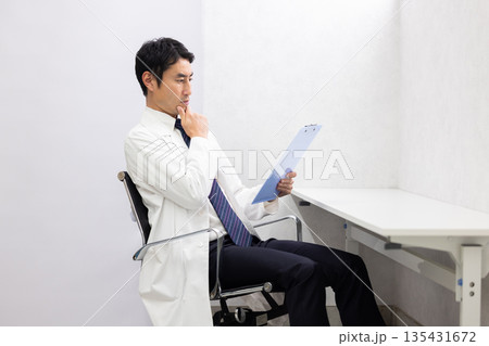 真剣な表情でカルテを読む白衣姿の男性医師 真剣な表情でカルテを読む白衣姿の男性医師 135431672