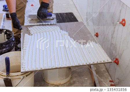 Worker applies adhesive on tile for installation in construction site Worker applies adhesive on tile for installation in construction site 135431856