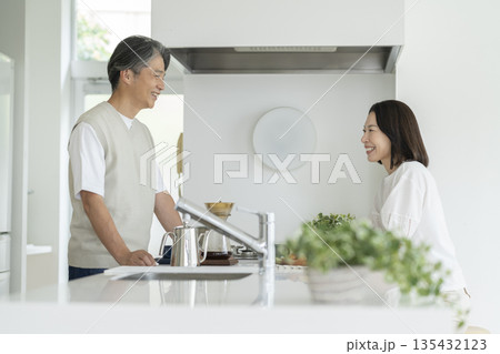 キッチンのカウンターを挟んで話をする笑顔の50代の夫婦 135432123