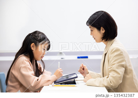 塾の先生に勉強を教わる小学生の女の子 塾の先生に勉強を教わる小学生の女の子 135432387