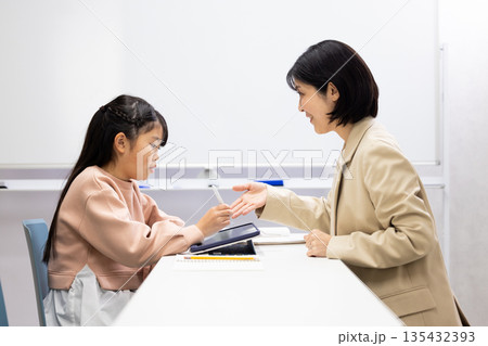 塾の先生に勉強を教わる小学生の女の子 塾の先生に勉強を教わる小学生の女の子 135432393