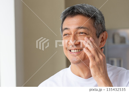 笑顔で頬に手をあてるシニアの男性 135432535