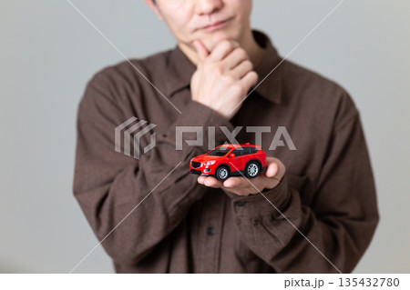 自動車の模型を持って悩むミドル男性 135432780