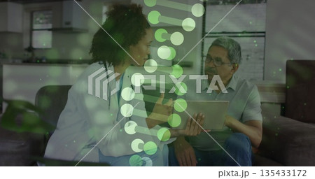 Pointing stethoscope doctor guiding senior patient with tablet on home sofa, with DNA helix overlay 135433172