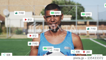 Standing male in blue sleeveless top holding soccer ball on soccer field, with social media icons 135433372