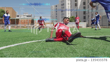 Sliding soccer player in red performing tackle on turf pitch, with chain-link fence and goal net 135433378