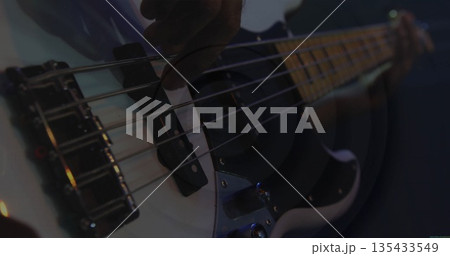 Plucking musician's hand exploring white electric bass strings on dim stage, with colored lights 135433549