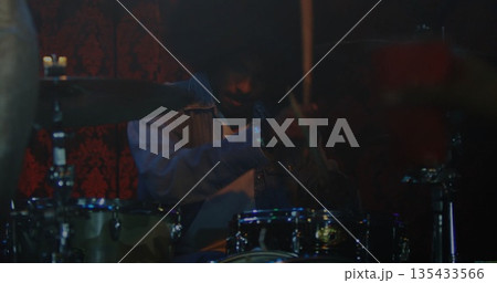 Playing Indian drummer hitting drums and cymbals on club stage, with denim jacket and drumsticks 135433566