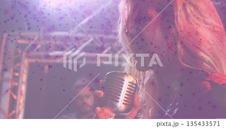 Singing female vocalist holding vintage microphone on dim stage, with electric guitar and truss Singing female vocalist holding vintage microphone on dim stage, with electric guitar and truss 135433571