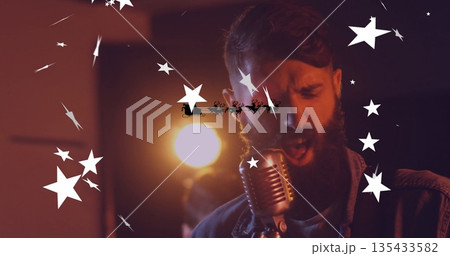 Leaning denim-clad singer into mic on stage in spotlight with Santa sleigh silhouette and overlays 135433582