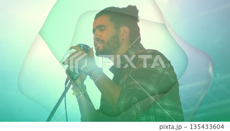 Performing male singer holding retro microphone on stand at concert stage, wearing plaid shirt 135433604