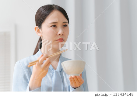 美味しくない表情でご飯を食べる女性 美味しくない表情でご飯を食べる女性 135434149
