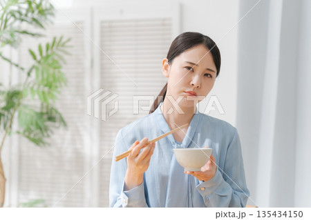 美味しくない表情でご飯を食べる女性 135434150