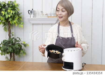 ノンフライヤーでおやつのポテトチップスを作るシニア女性 135434354