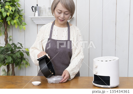 ノンフライヤーでおやつのポテトチップスを作るシニア女性 ノンフライヤーでおやつのポテトチップスを作るシニア女性 135434361