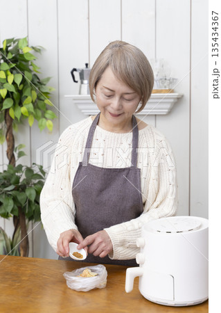 ノンフライヤーでおやつのポテトチップスを作るシニア女性 135434367
