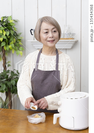 ノンフライヤーでおやつのポテトチップスを作るシニア女性 135434368