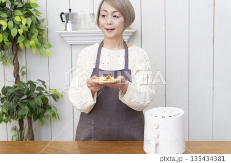 ノンフライヤーでおやつのポテトチップスを作るシニア女性 135434381