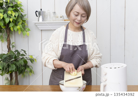 ノンフライヤーでおやつのポテトチップスを作るシニア女性 ノンフライヤーでおやつのポテトチップスを作るシニア女性 135434392