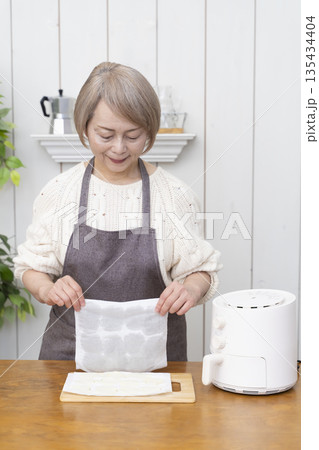 ノンフライヤーでおやつのポテトチップスを作るシニア女性 135434404