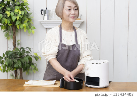 ノンフライヤーでおやつのポテトチップスを作るシニア女性 135434408