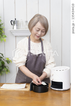 ノンフライヤーでおやつのポテトチップスを作るシニア女性 135434410