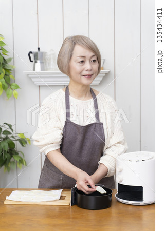 ノンフライヤーでおやつのポテトチップスを作るシニア女性 135434411