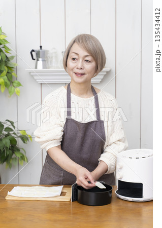 ノンフライヤーでおやつのポテトチップスを作るシニア女性 135434412