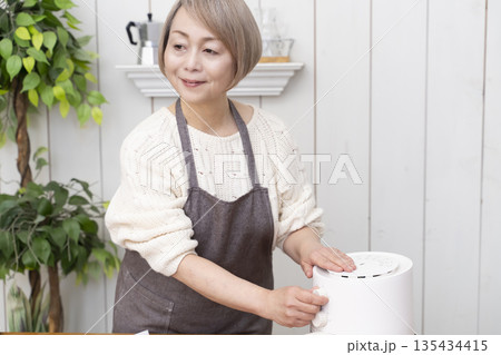 ノンフライヤーでおやつのポテトチップスを作るシニア女性 135434415