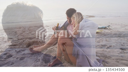 Couple wrapping blanket, sipping bottles on dusk beach with surfboard, senior overlay, copy space Couple wrapping blanket, sipping bottles on dusk beach with surfboard, senior overlay, copy space 135434500