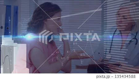 Patient and doctor in scrubs discussing symptoms at consultation desk, with digital charts 135434588