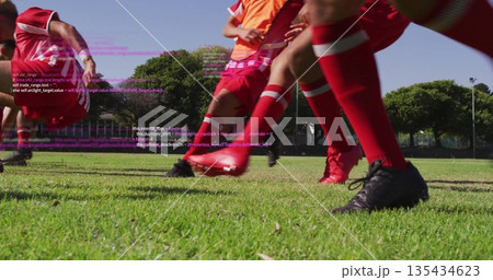 Sprinting soccer players wearing red uniforms, cleats on field at park with orange bib code overlay Sprinting soccer players wearing red uniforms, cleats on field at park with orange bib code overlay 135434623