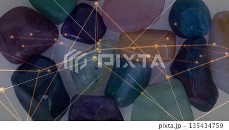 Displaying polished multicolored gemstones arranged on white tabletop, with golden network overlay 135434759