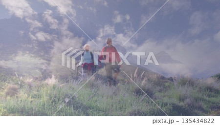Hiking mature couple walking hand in hand through wildflower meadow, with backpacks, trekking poles Hiking mature couple walking hand in hand through wildflower meadow, with backpacks, trekking poles 135434822