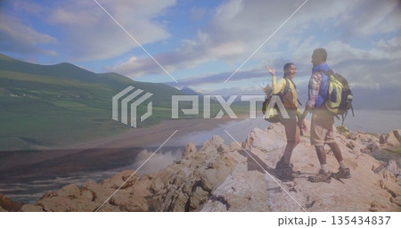 Waving hikers overlooking beach on headland, with neon green backpacks and hiking boots, copy space 135434837