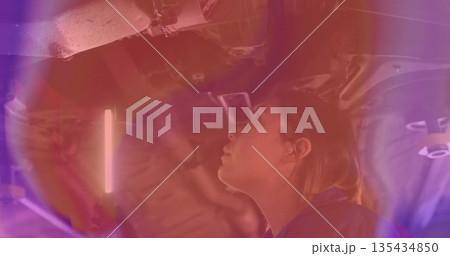 Working female technician in coveralls inspecting underside at garage, under fluorescent work light 135434850