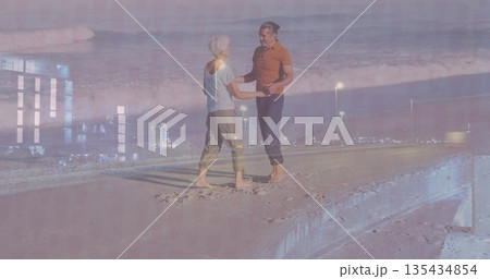 Standing barefoot couple holding hands on sandy concrete pier at dusk, with lamp posts, ocean waves 135434854
