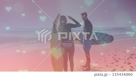 Standing woman and man wearing swimwear holding surfboards at beach, with heart-shaped lights Standing woman and man wearing swimwear holding surfboards at beach, with heart-shaped lights 135434860