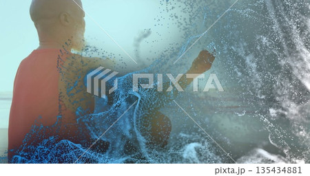 Sitting man wearing orange tee gazing toward horizon on sandy beach, with digital bits, copy space 135434881