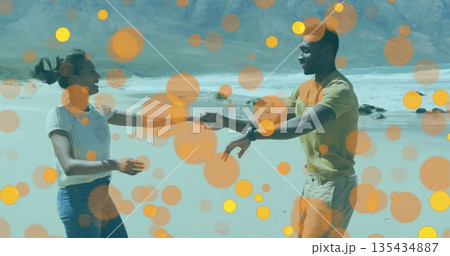 Holding hands and dancing couple on sandy shoreline next to ocean waves, with wristwatch, bokeh 135434887