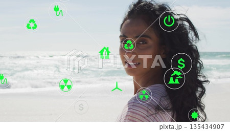 Standing woman wearing striped top glancing back on beach, floating environmental icons, copy space 135434907