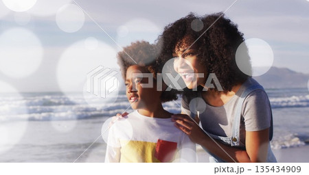 Gazing mother and son sharing moment facing horizon at sandy beach shoreline, with soft lens flares 135434909