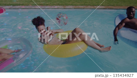 Laughing woman wearing swimsuit in yellow tube at poolside, with white tube, pink tube, beach ball Laughing woman wearing swimsuit in yellow tube at poolside, with white tube, pink tube, beach ball 135434927