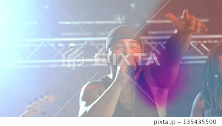 Gripping microphone, singer reaching out on stage under metal truss with lights and guitar neck 135435500