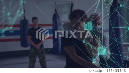 Demonstrating instructor applying hold on student in martial arts dojo with punching bags and mats 135435548