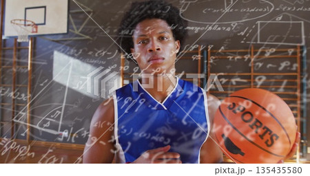 Standing athlete in blue jersey holding basketball labeled SPORTS on school gym court, math overlay Standing athlete in blue jersey holding basketball labeled SPORTS on school gym court, math overlay 135435580
