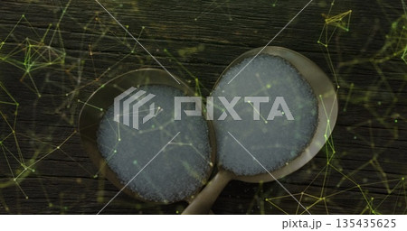 Showing two steel spoons holding granulated sugar on wood counter, featuring green-yellow overlay Showing two steel spoons holding granulated sugar on wood counter, featuring green-yellow overlay 135435625
