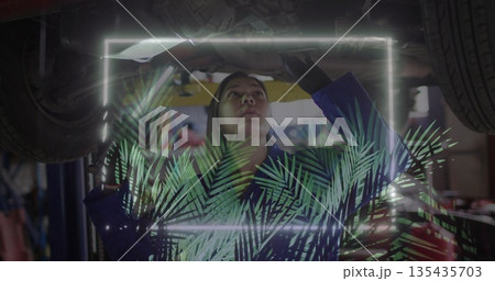 Inspecting mechanic in coveralls examining engine on hydraulic lift in shop, neon frame overlay 135435703